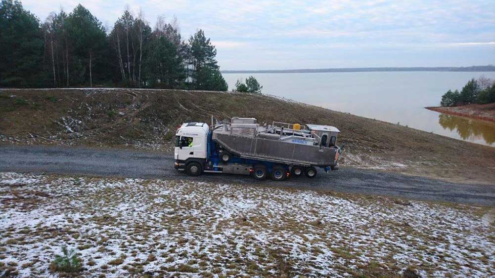 A truck by a lake with a small boat on the cargo area.